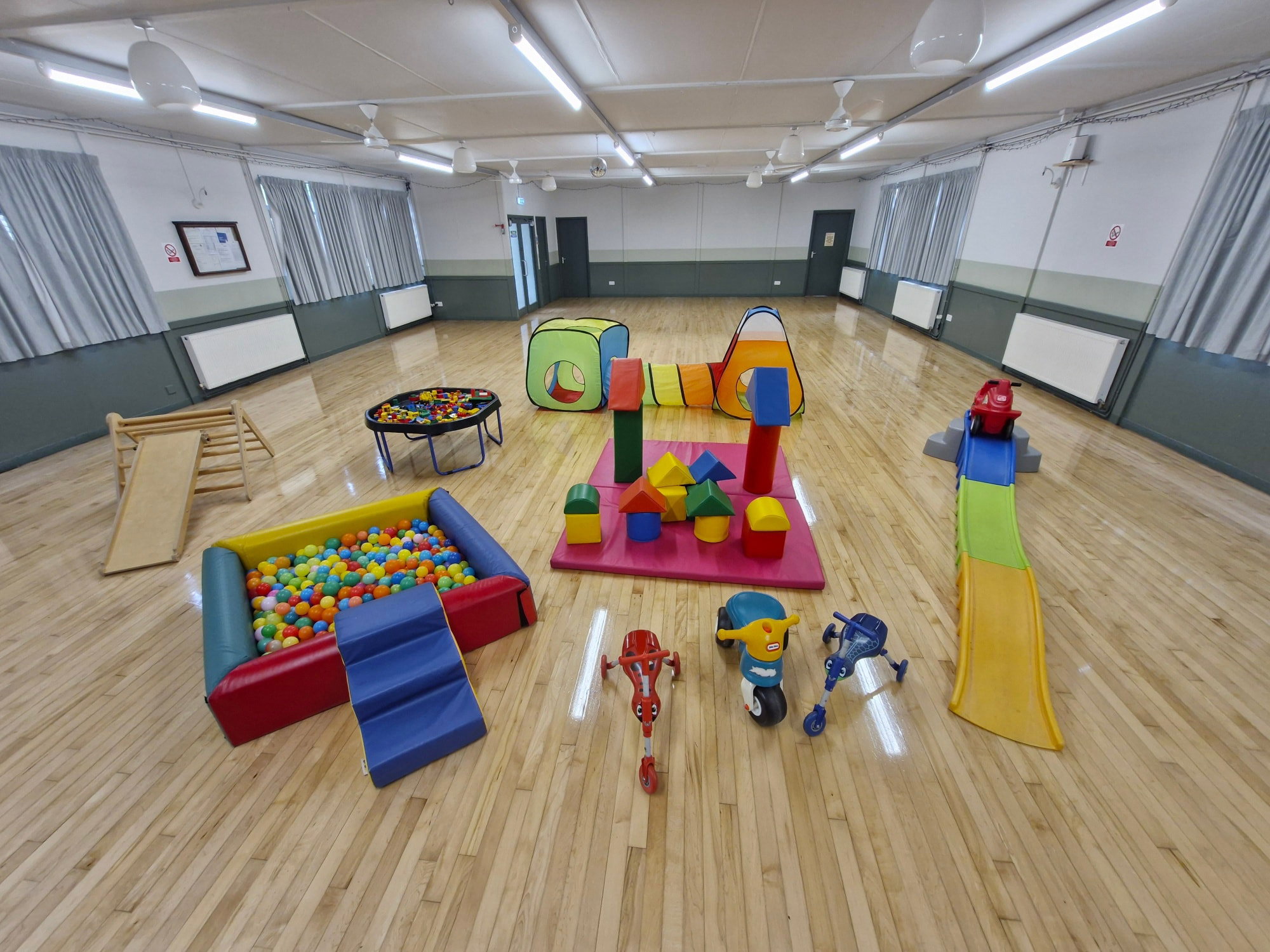 A hall set up for a Stay & Play session with a ball pool, soft play, tunnels and ride-on toys